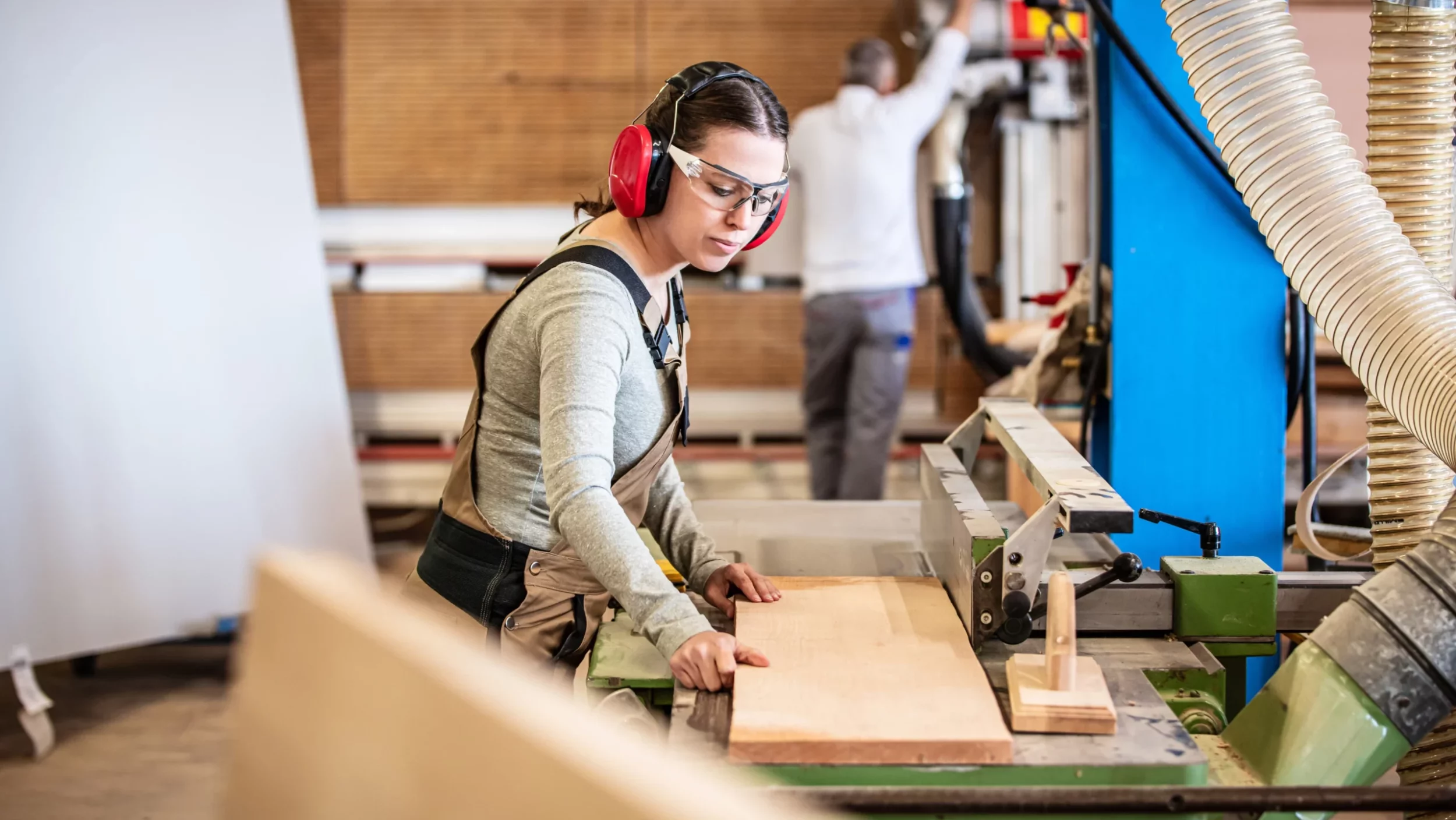 Schreiner:innen bei der Arbeit, die Frau im Vordergrund arbeitet in einer Werkstatt mit Holz