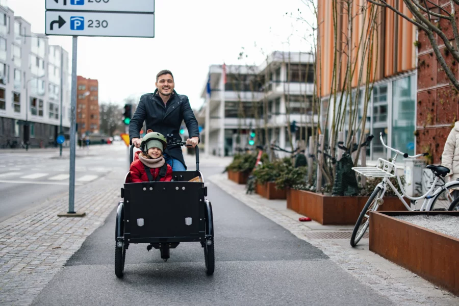 Junger Mann fährt mit einem Kind auf einem Lastenrad.