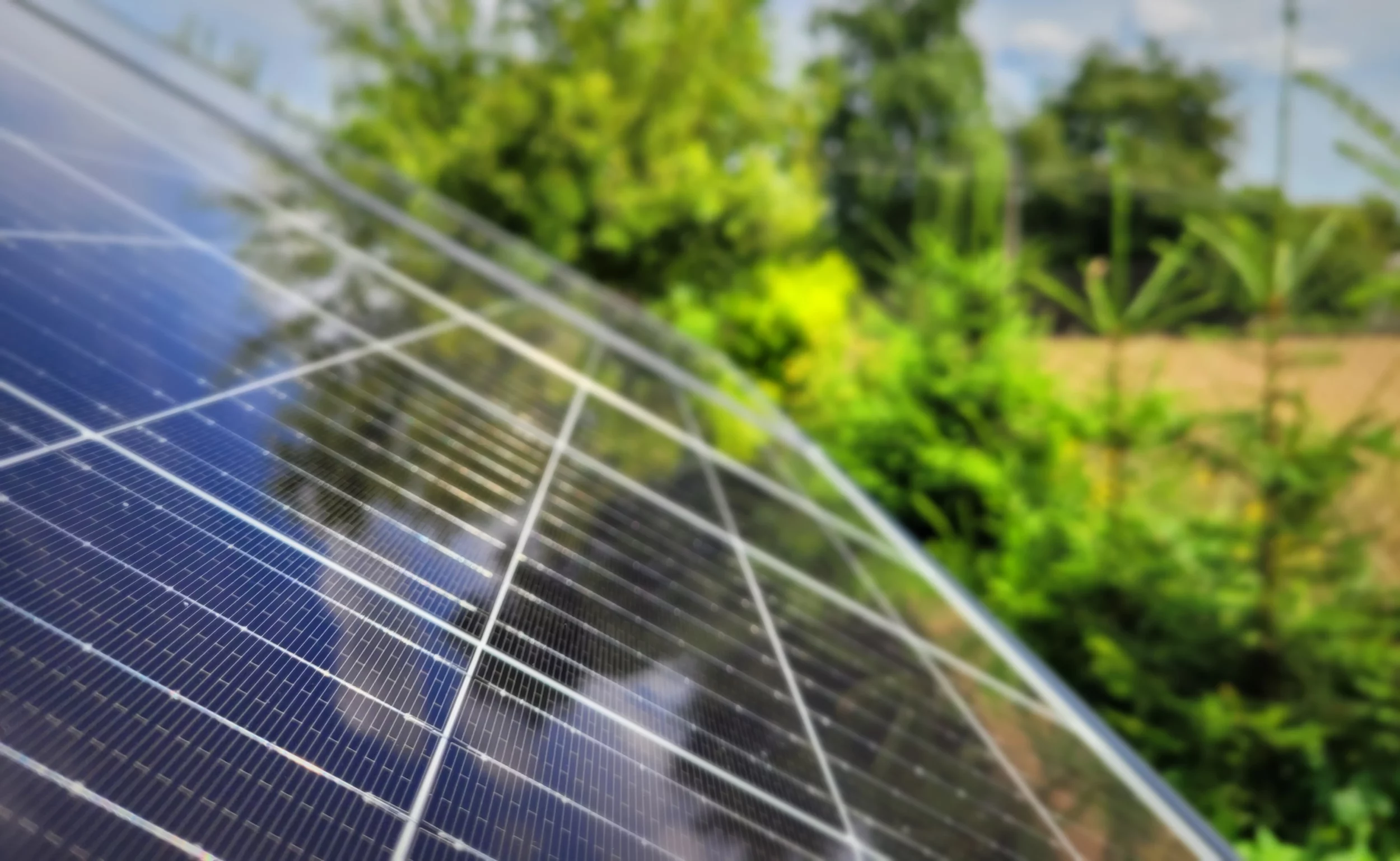 Photovoltaik-Dachanlage zur Erzeugung erneuerbarer und ökologischer Solarenergie, im Hintergrund Bäume, Feld, Himmel