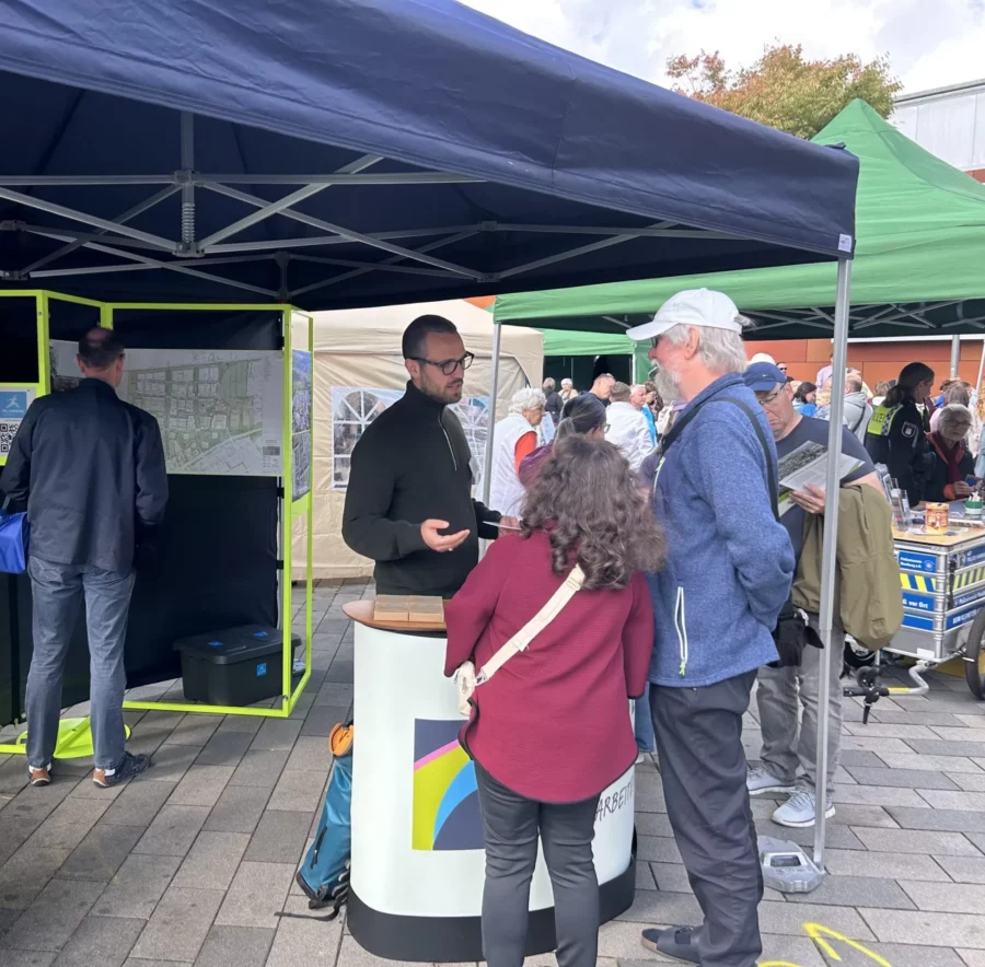 Menschen im Gespräch an einem Infostand zur Quartiersentwicklung.