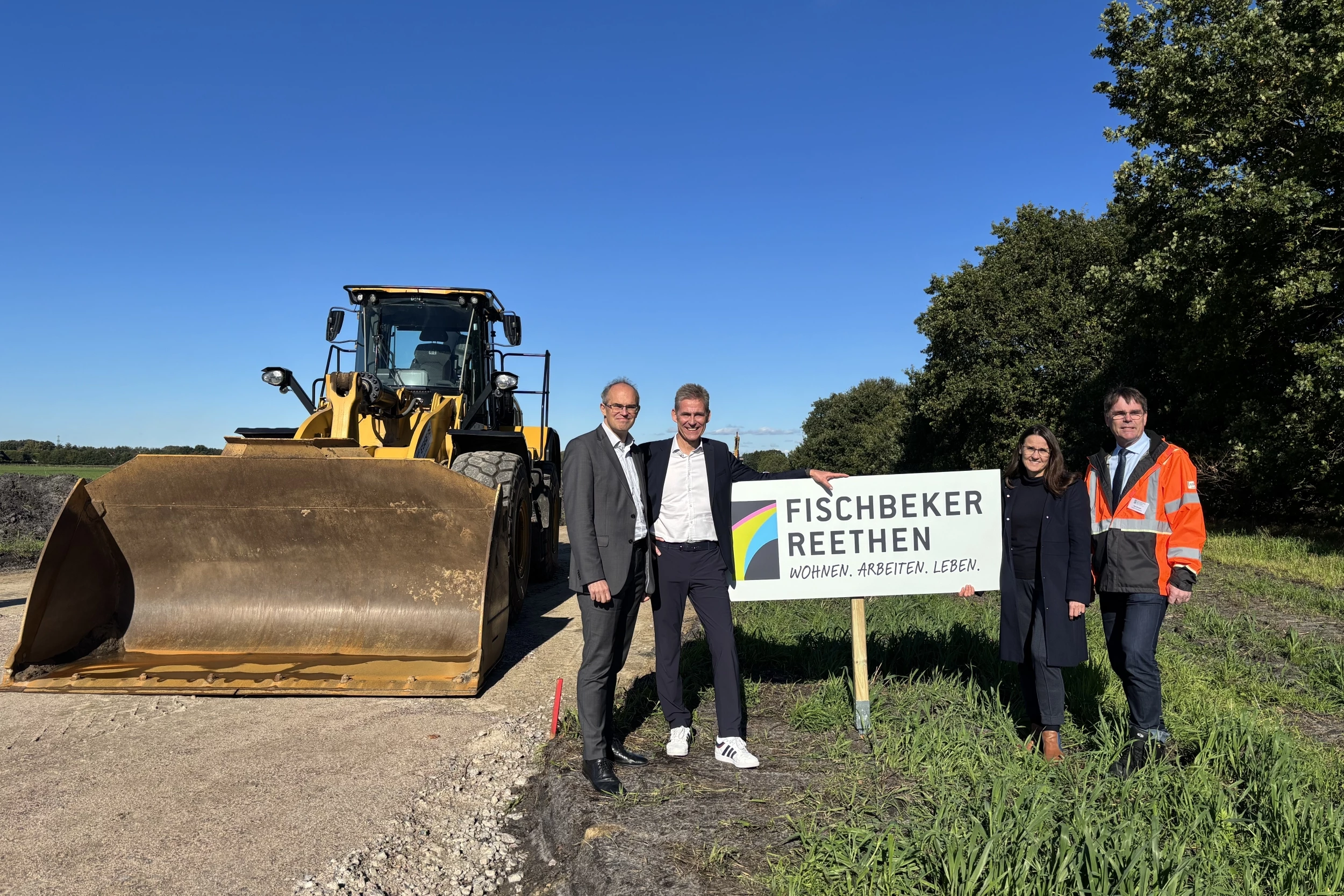 Christian Carstensen, Kay Gätgens, Karen Pein, René Herrmann stehen um ein Schild mit der Aufschrift "Fischbeker Reethen", im Hintergrund eine große Baumaschine und Ackerland
