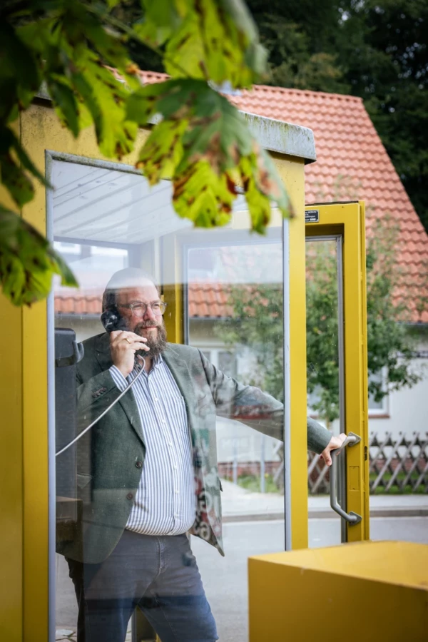 Stefan Zimmermann simuliert einen Anruf in einer gelben Telefonzelle